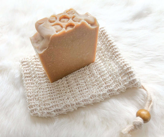 Soap saver bag made of natural sisal, holding a bar of soap, used for exfoliating skin and keeping soap dry in the shower.